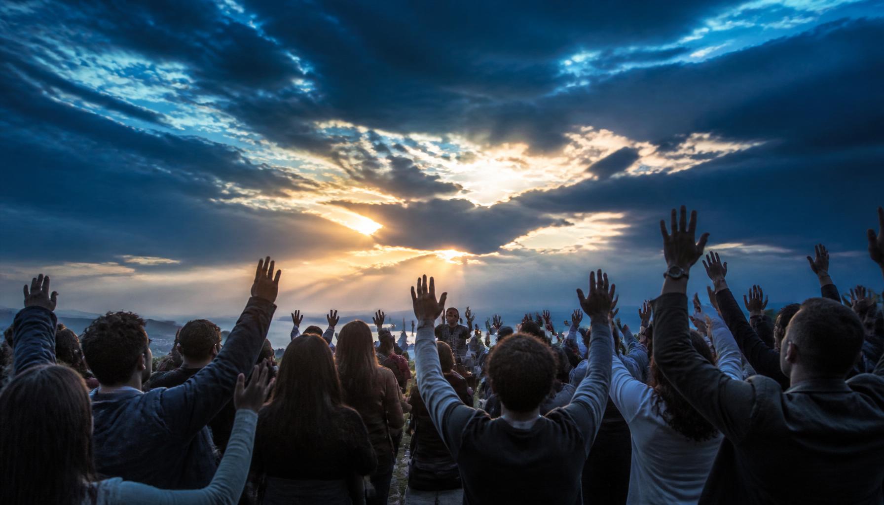 Diverse people worshipping with raised hands at dusk
